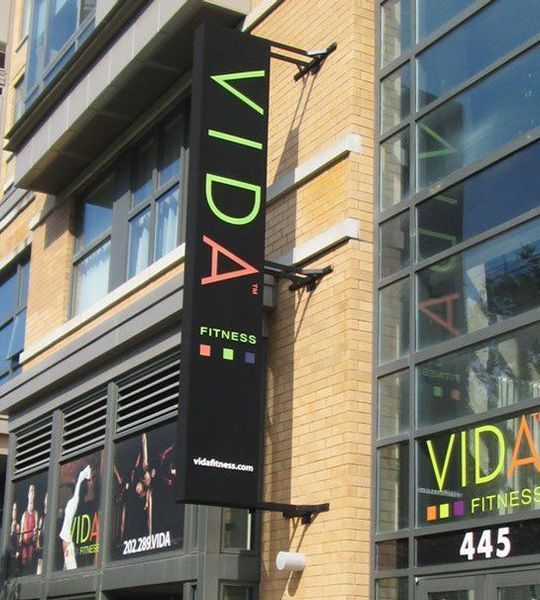 Sign for VIDA Fitness on a brick building; black banner with green, orange, and blue lettering.