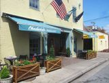 Restaurant exterior with teal awnings, an American flag, and potted plants.