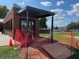 Brick building entrance with a ramp, orange safety fencing, and construction cones.
