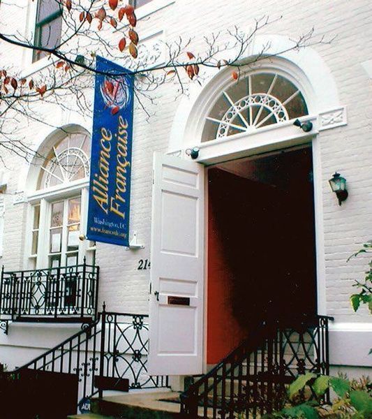 Exterior of the Alliance Française building in Washington, D.C. with open doors, banner, and ornate ironwork.