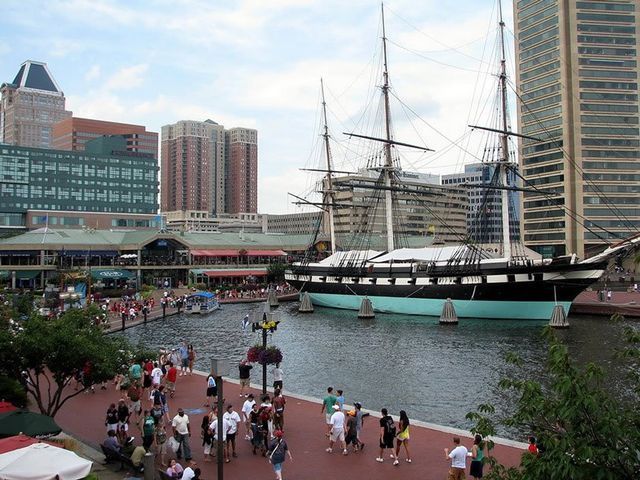 Waterfront scene with tall ship, people walking, and buildings in Baltimore.
