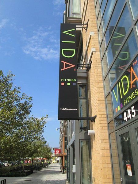 Sign for Vida Fitness with black background, neon green letters, brick building.