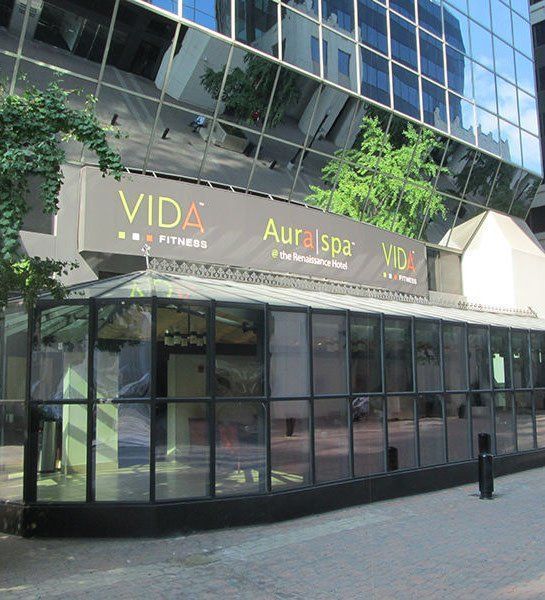 VIDA Fitness and Aura Spa storefront in a city with glass windows reflecting buildings.