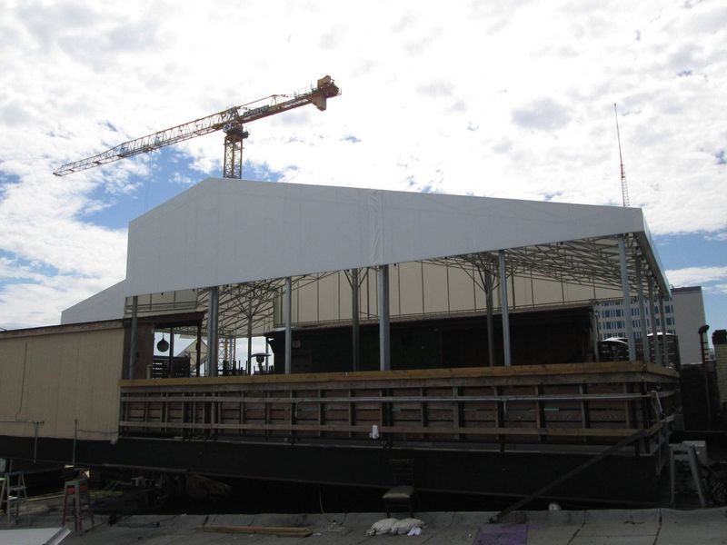 Building under construction with a crane in the background, featuring a white awning and exposed metal framing.