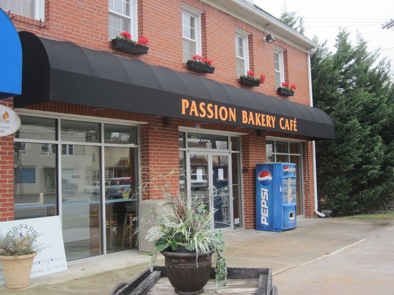 Passion Bakery Cafe storefront with black awning, brick building, and Pepsi machine.