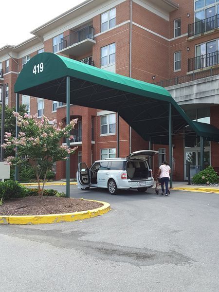 A covered entrance with a white van. Person loading bags. Building with balconies in background.