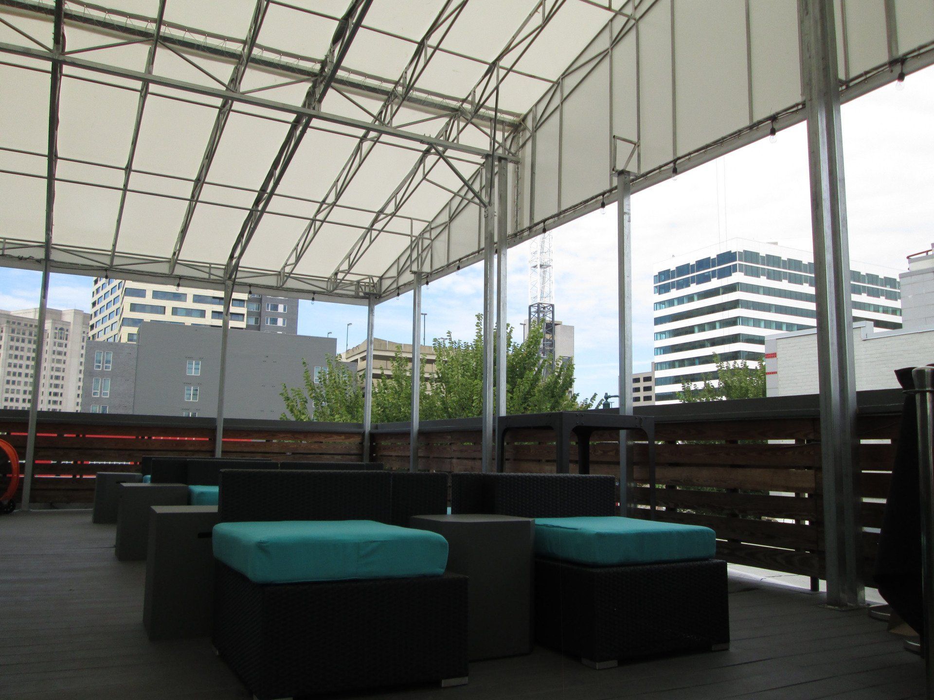 Outdoor seating area with canopy, overlooking city buildings. Turquoise cushions, neutral furniture, and wood accents.