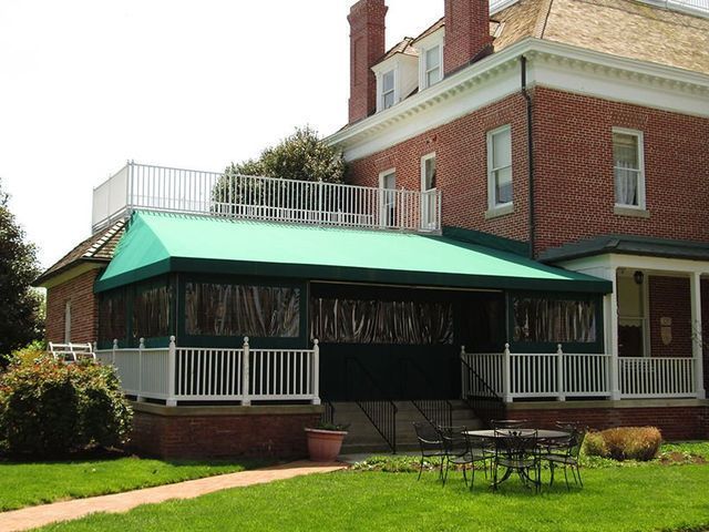 A brick building with a green awning-covered porch, white railing, and a rooftop deck.