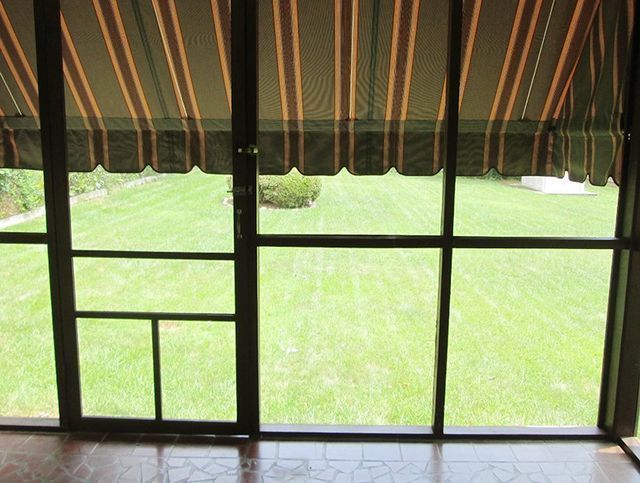 View through a screen door of a green lawn with an awning overhead.