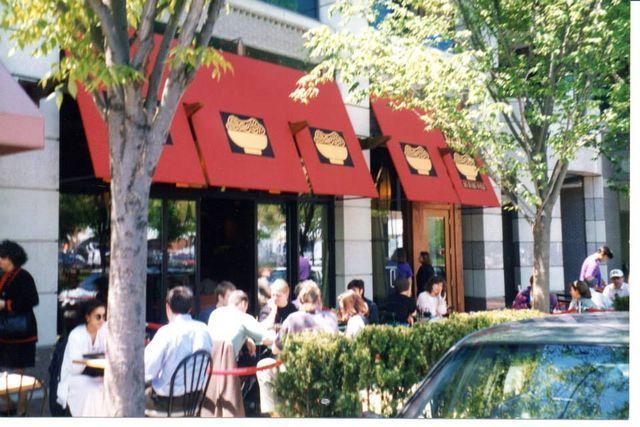 Restaurant exterior with red awnings, outdoor seating, and people dining.