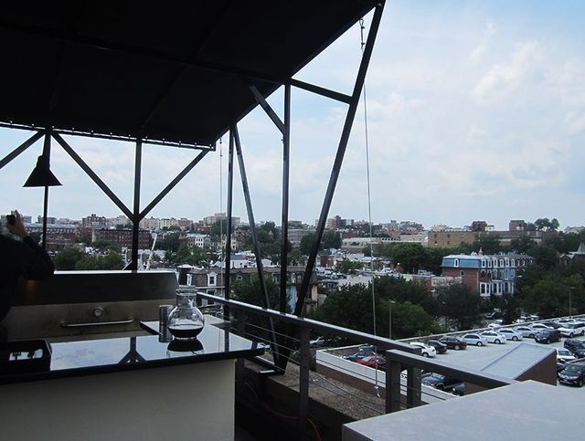 Rooftop view: black metal structure with cityscape, parking lot, and cloudy sky.
