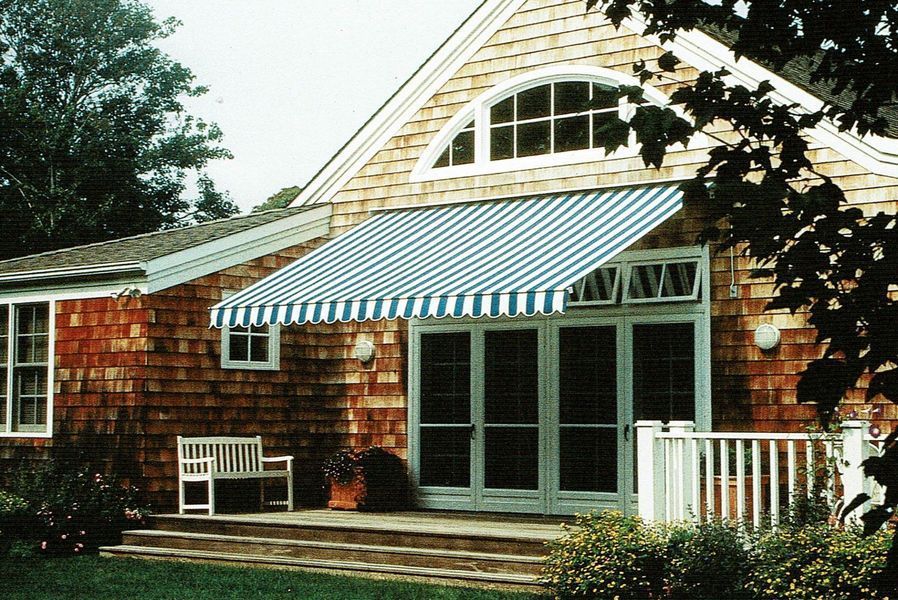 House with a blue and white striped awning over a set of glass doors and a wooden deck.