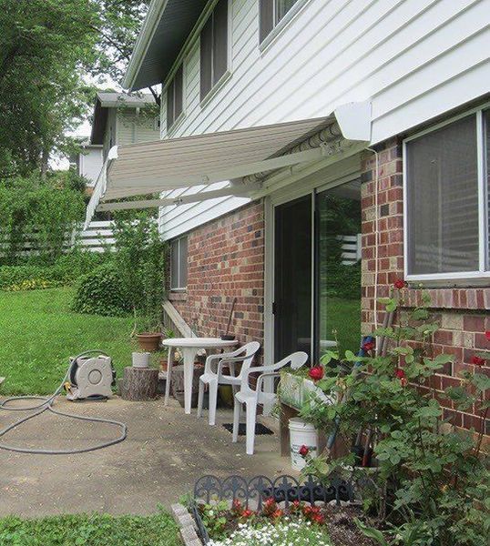 Backyard patio with an awning, chairs, table, and sliding glass door on a brick building.