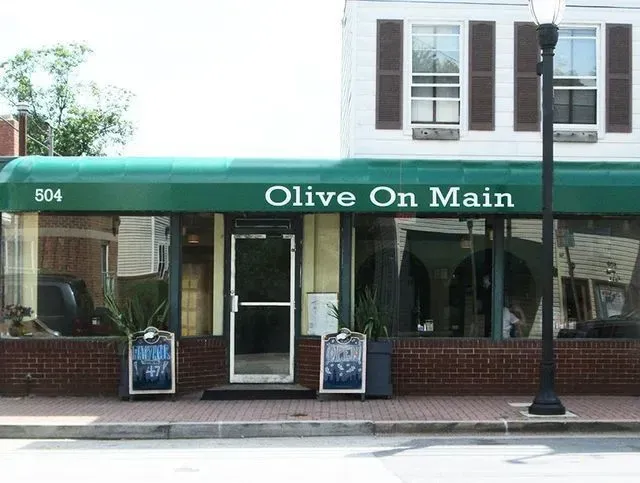 Olive On Main restaurant storefront with green awning, brick facade, and street lamp.