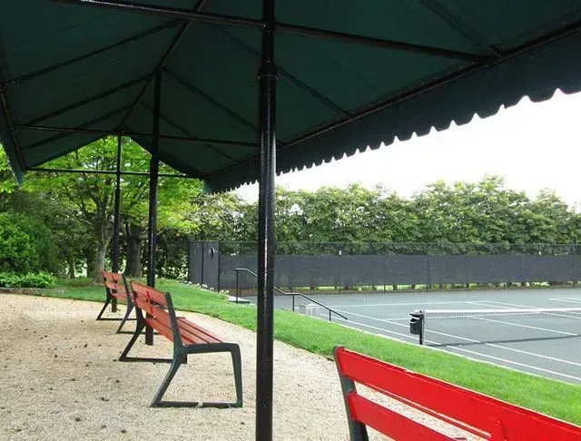 Tennis court viewing area with benches under a green canopy.