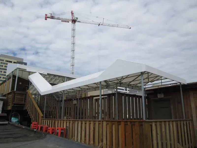 Outdoor patio with white canopy, wooden deck and fence, crane in background.
