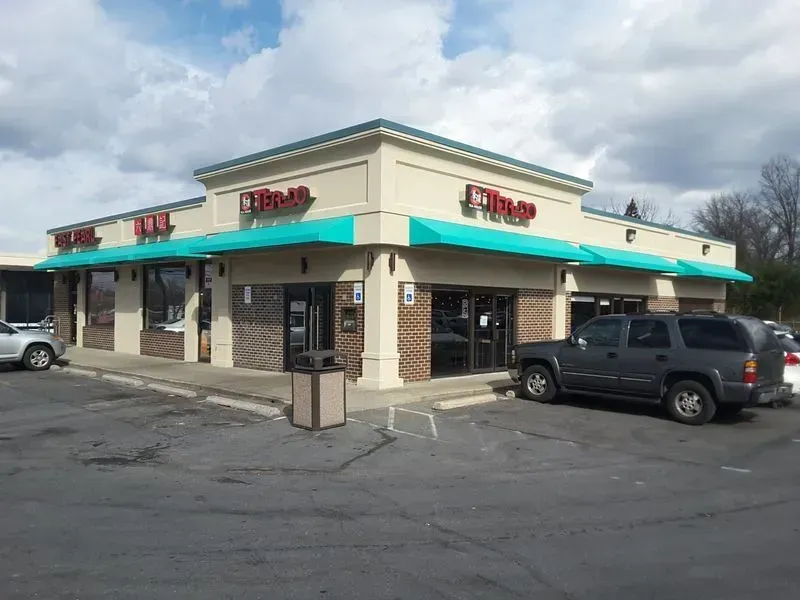 A corner building with a light beige exterior and teal awnings, with signage reading 