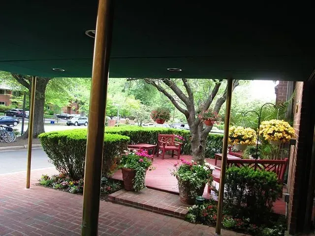 Outdoor seating area with brick, greenery, flowers, and a tree.