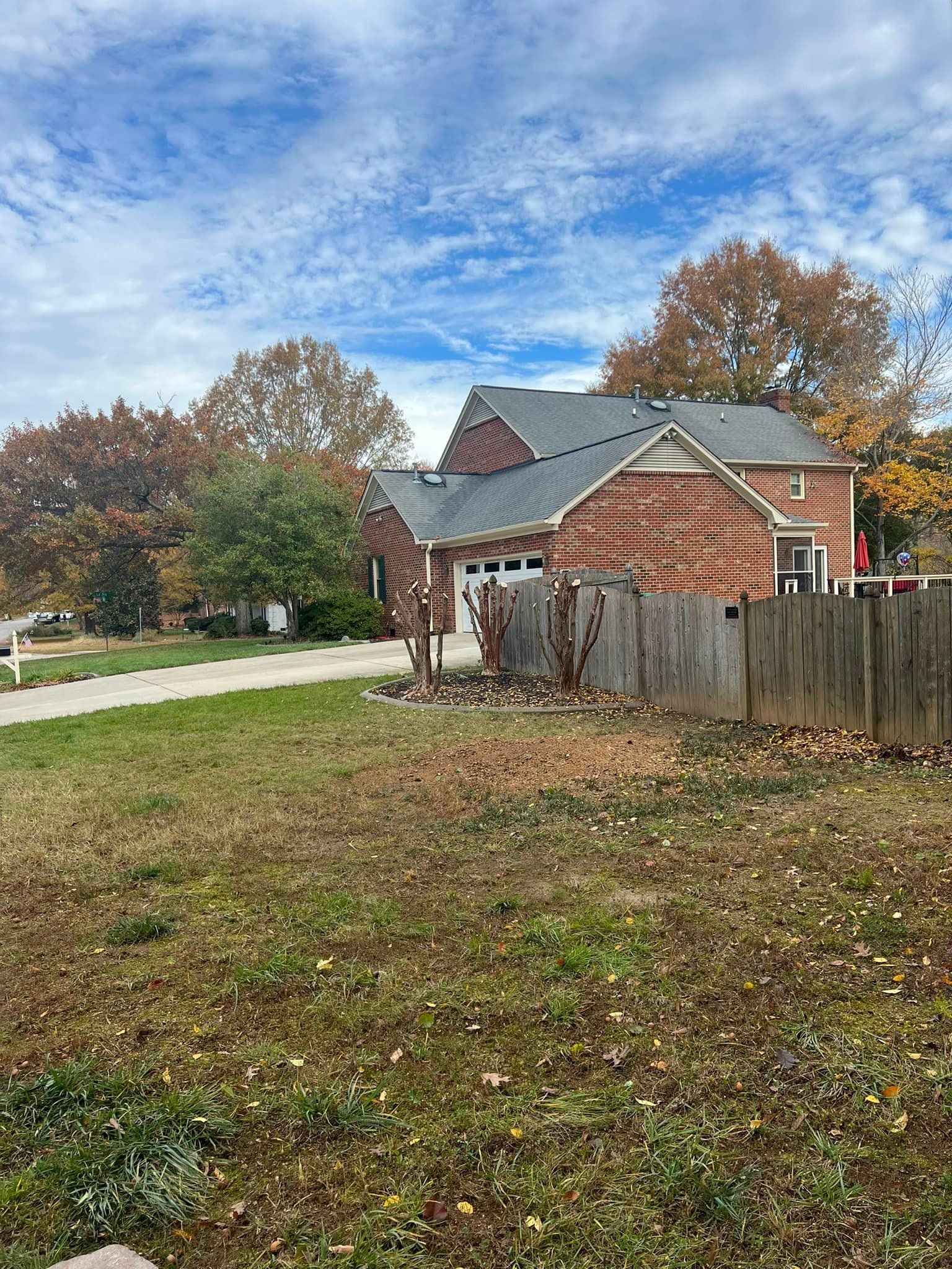 Suburban house with red brick exterior, brown fence, fall trees, and blue sky.
