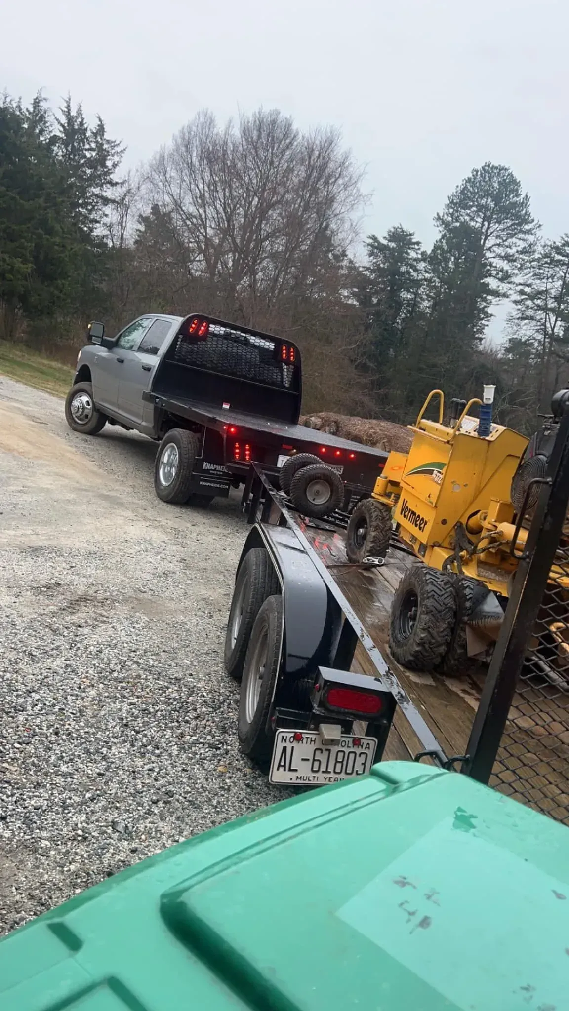 Gray pickup truck towing a trailer with construction equipment on a gravel road.