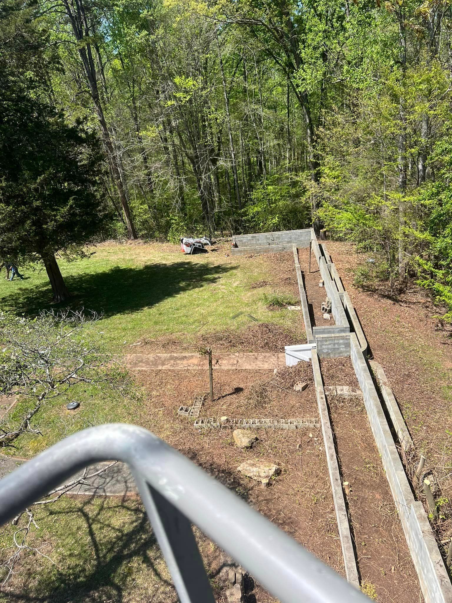 Overhead view of a backyard with a retaining wall and a forested backdrop.