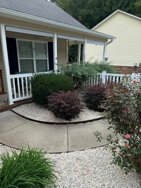 A front yard with a house, walkway, and bushes surrounded by white stones.