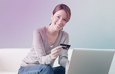 a woman is sitting on a couch holding a credit card and using a laptop computer