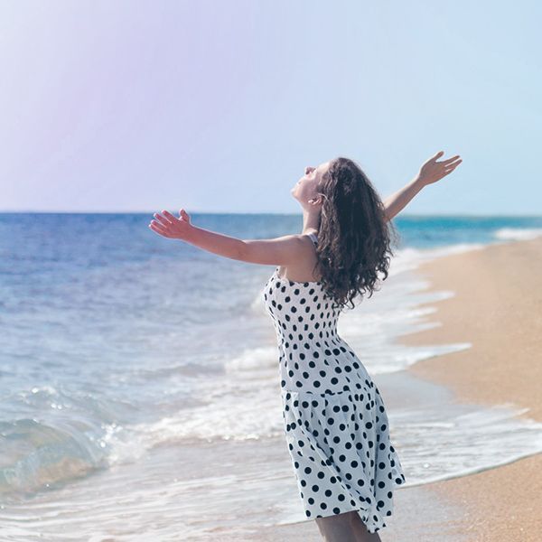 a woman in a polka dot dress is standing on the beach with her arms outstretched