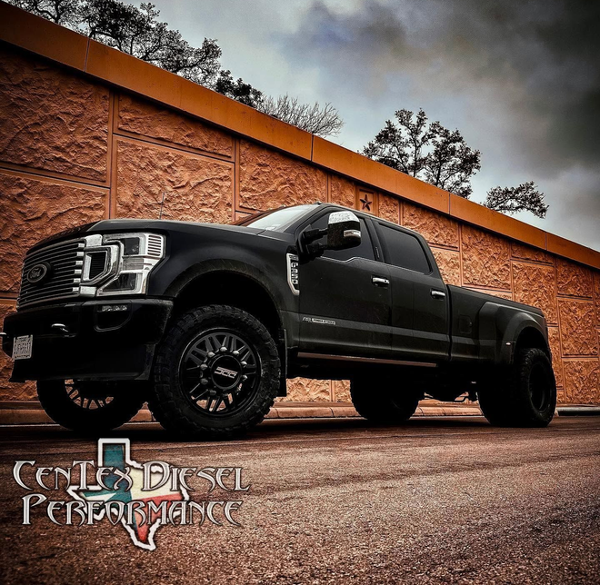 Black lifted pickup truck parked beside an orange wall under a cloudy sky