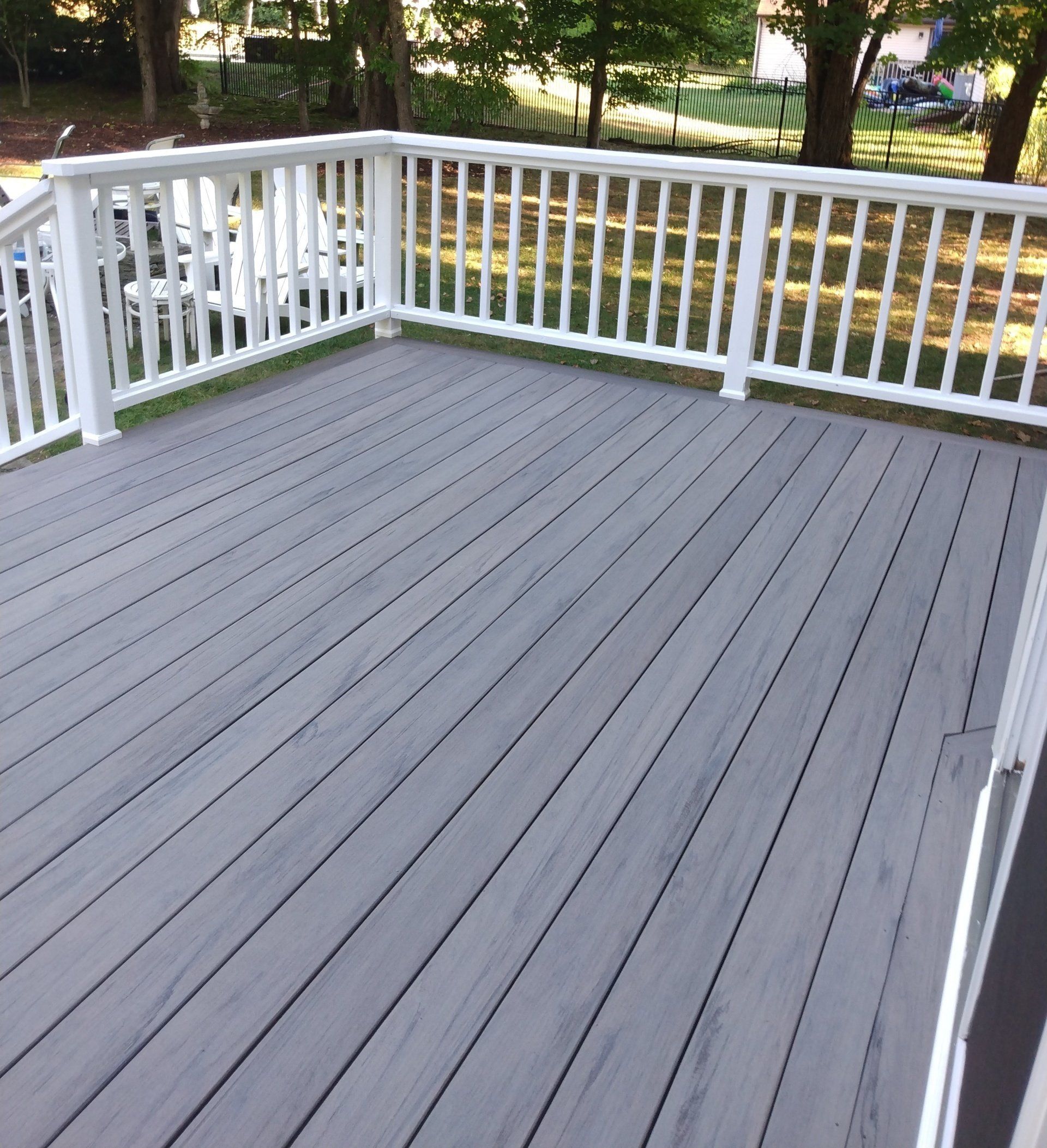 A gray deck with a white railing and trees in the background