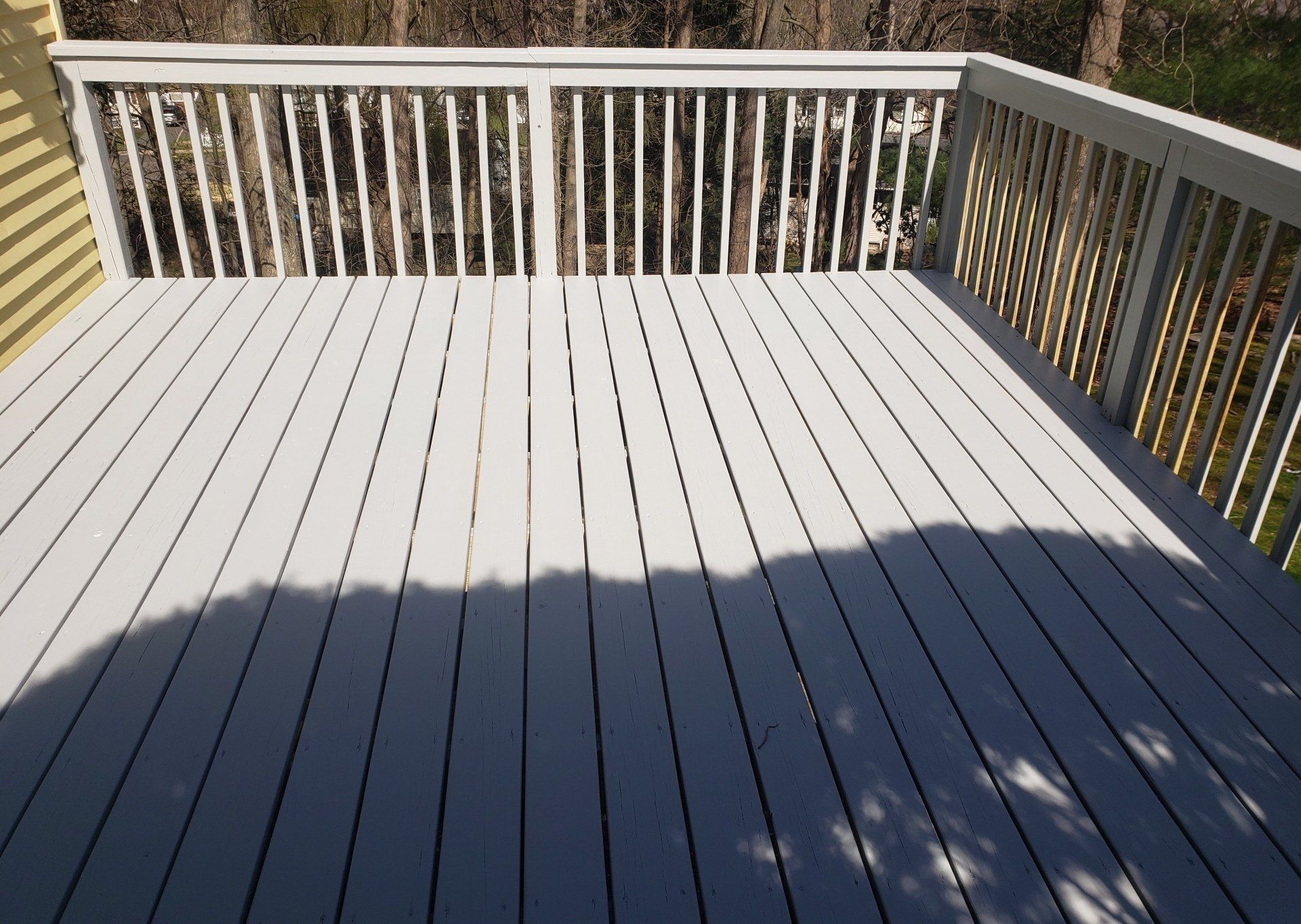 A white deck with a white railing and trees in the background.