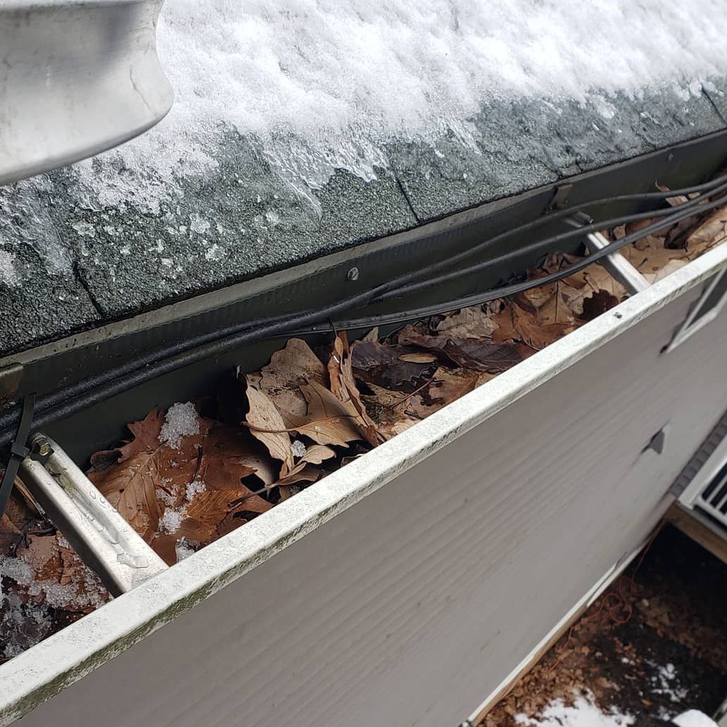 A gutter filled with leaves and snow on a roof