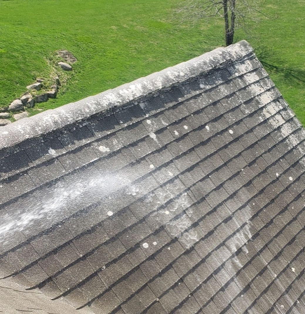 A roof is being cleaned with a pressure washer in a field.