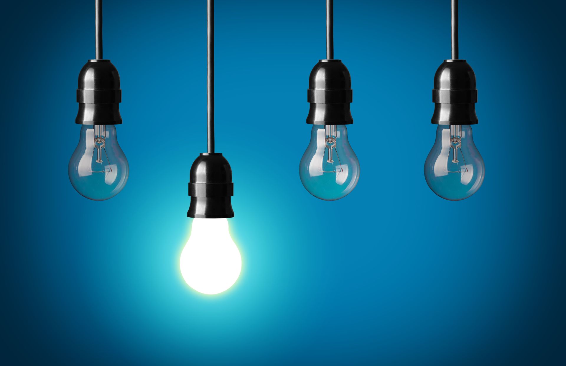 Four hanging light bulbs on a blue background, one glowing brightly.