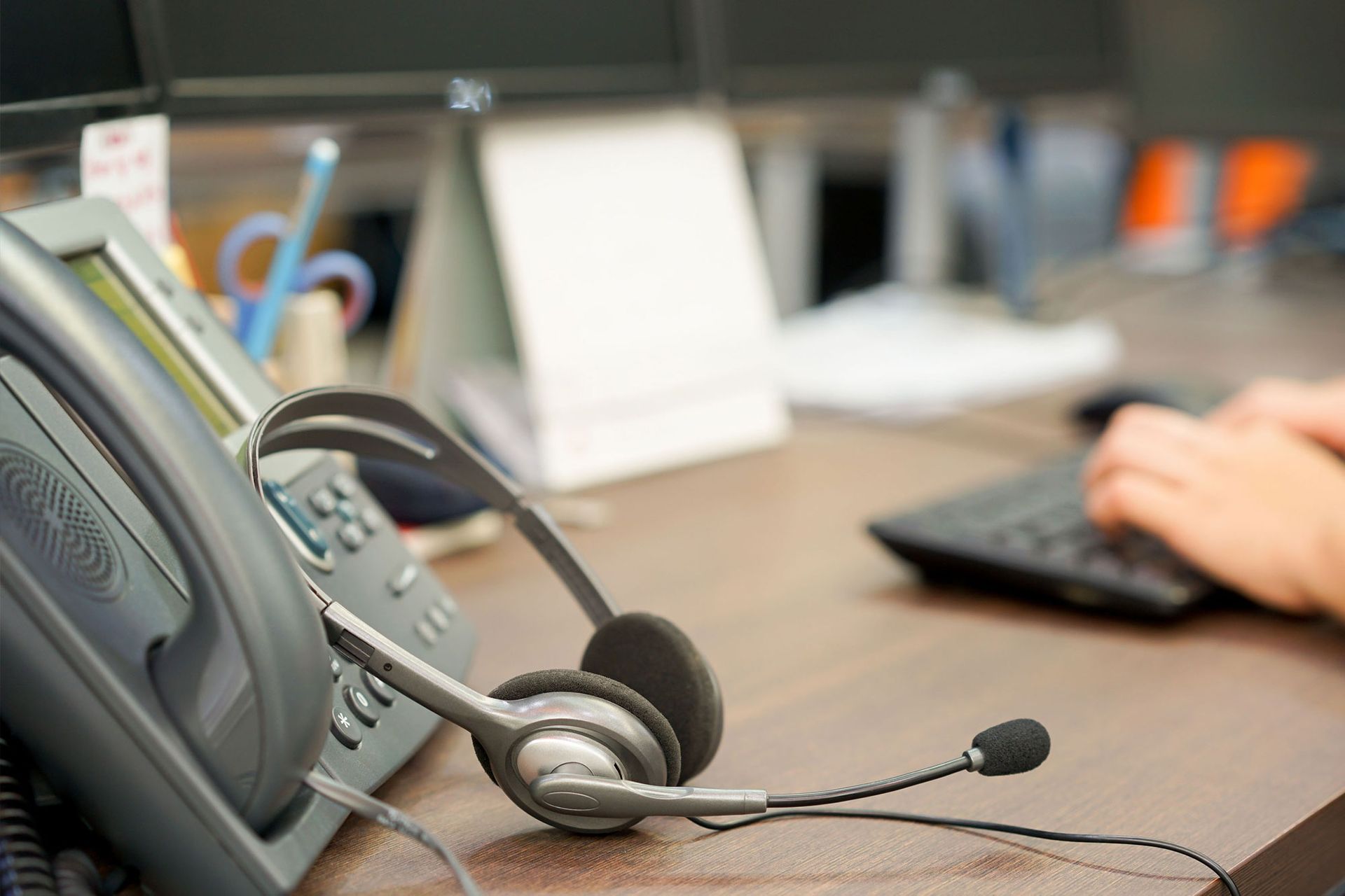Desk phone with headset on an office desk, with a hand using a computer keyboard in the background
