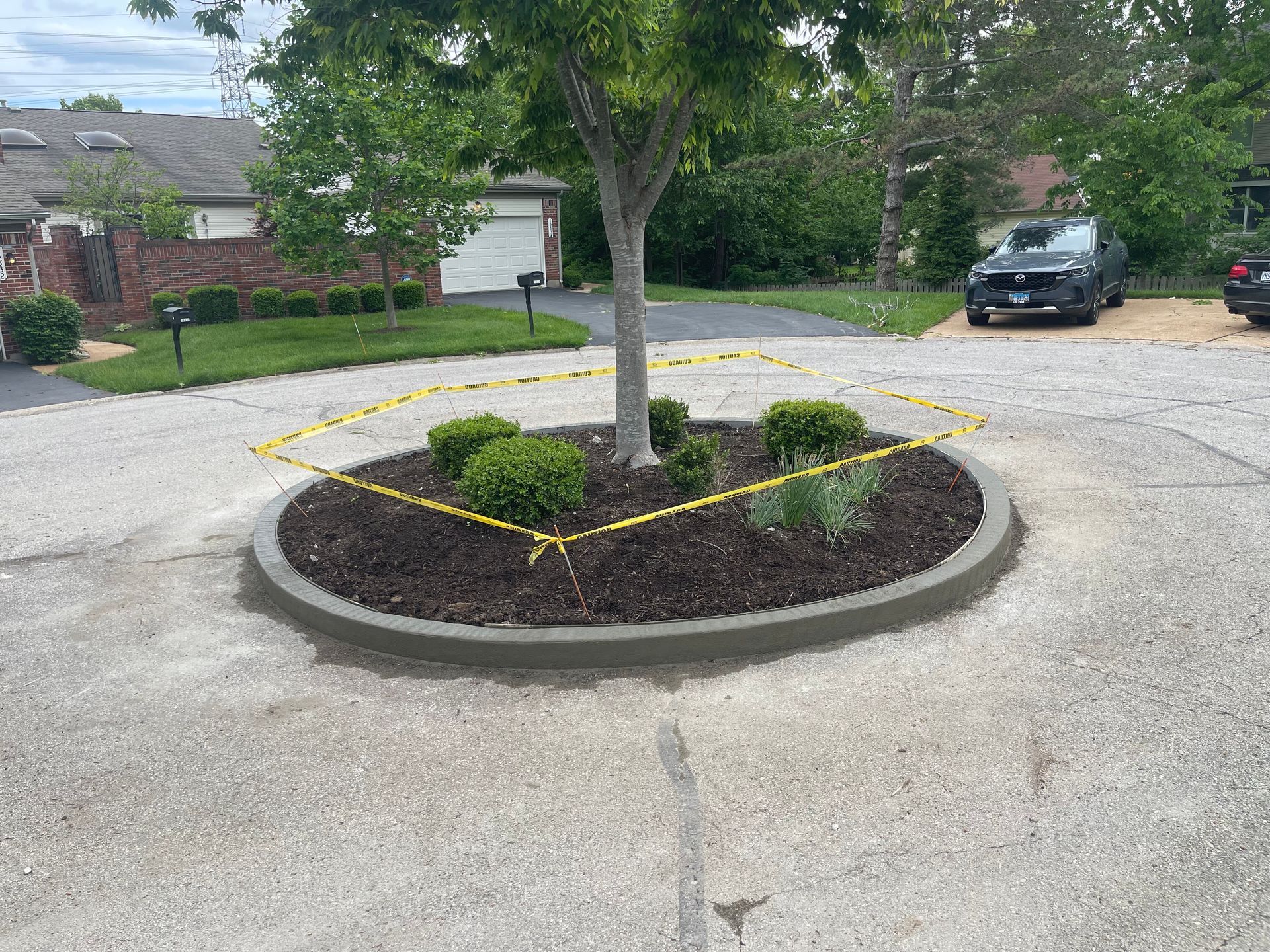 Circular landscaped tree island with dark mulch and shrubs in a residential driveway, with a parked car nearby