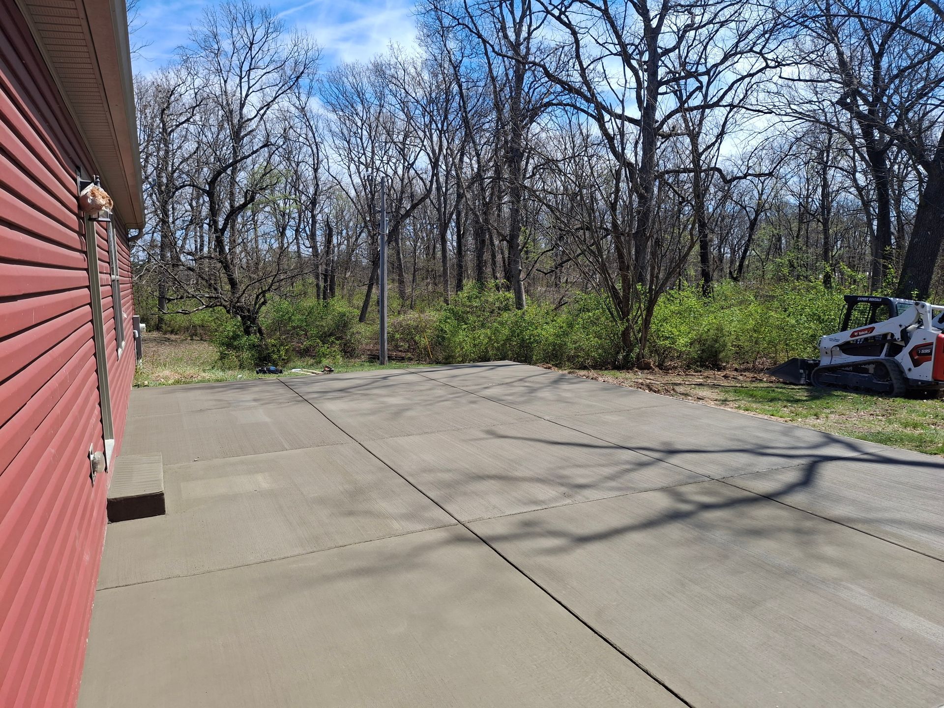 Concrete driveway beside a red building, with leafless trees and a small white utility vehicle at right.
