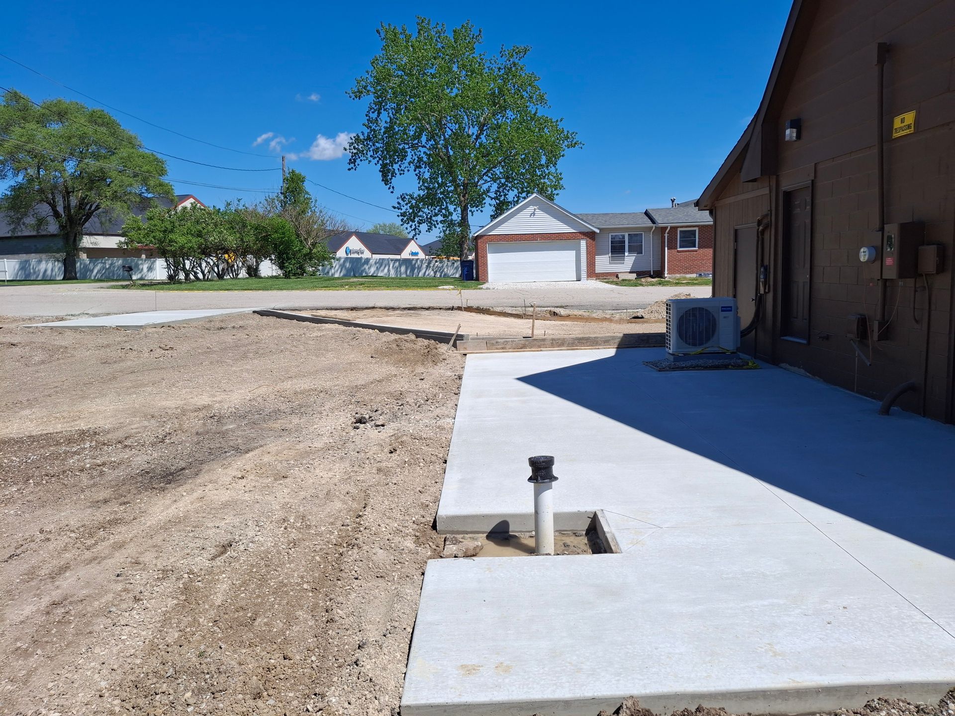 Fresh concrete driveway beside a brick house, with a dirt yard and suburban homes in the background.