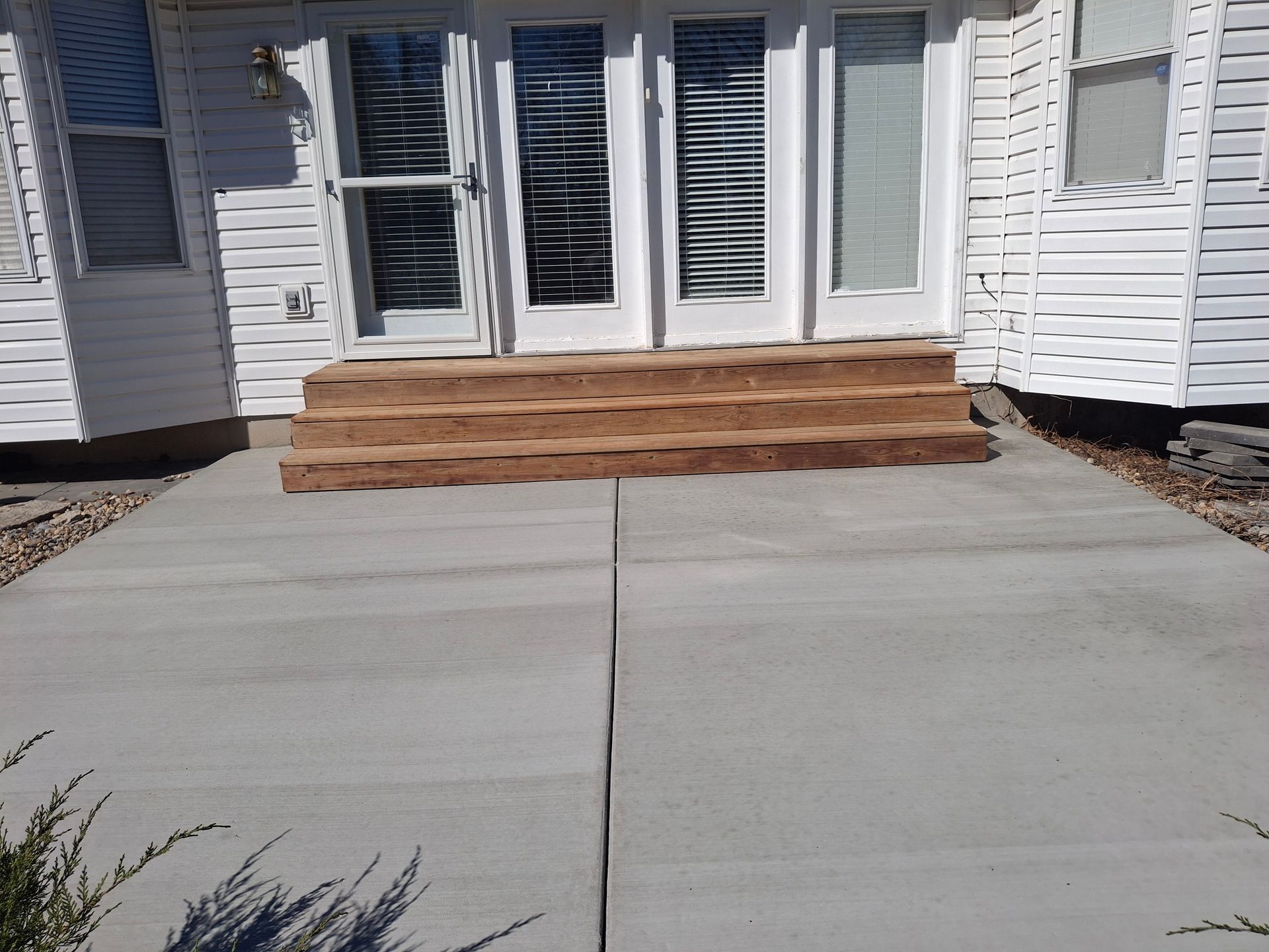 Front porch with white siding, glass doors, wooden steps, and a concrete driveway in front