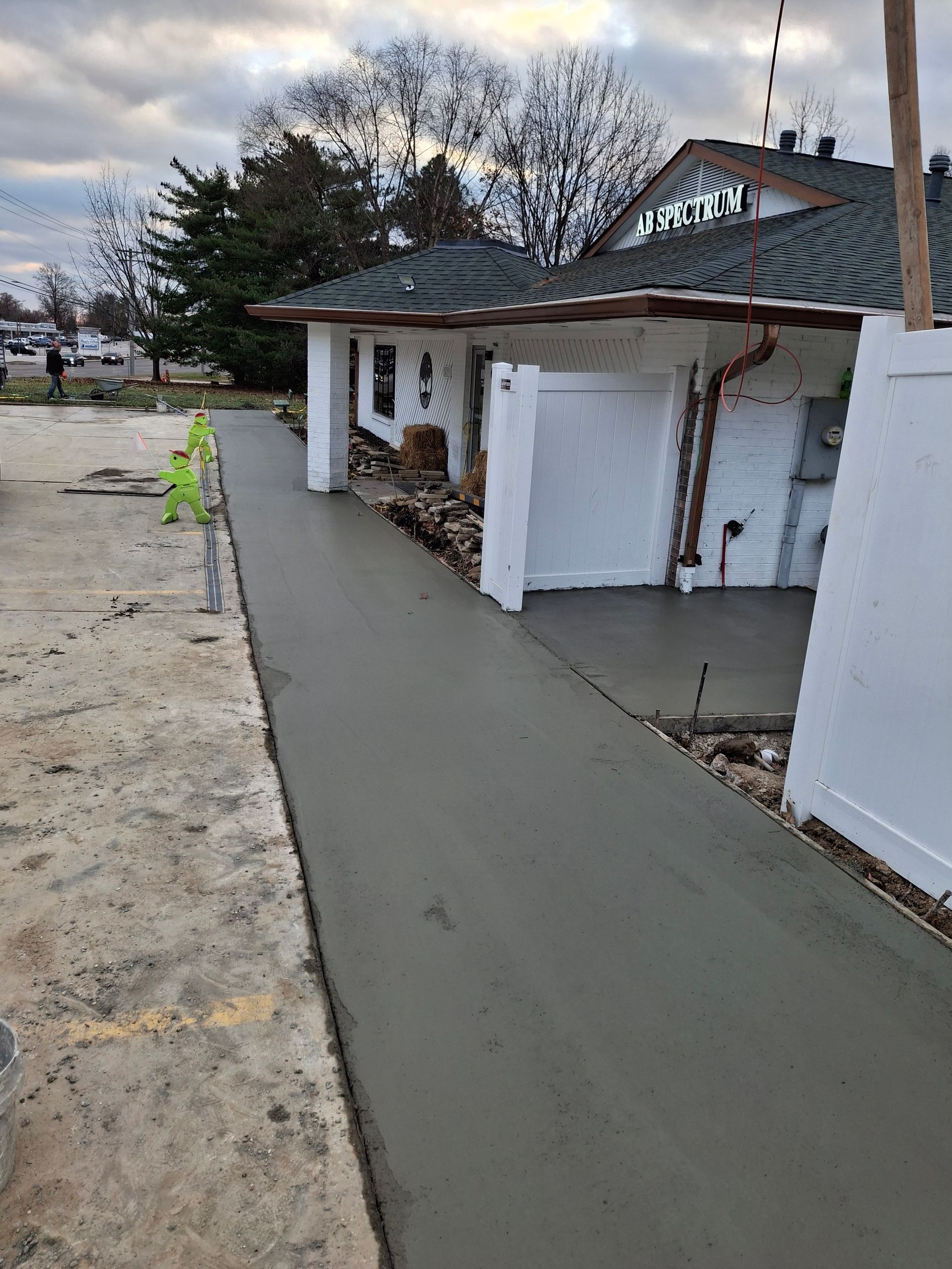 Fresh gray sidewalk beside a white building with green roof trim and a yellow caution sign.