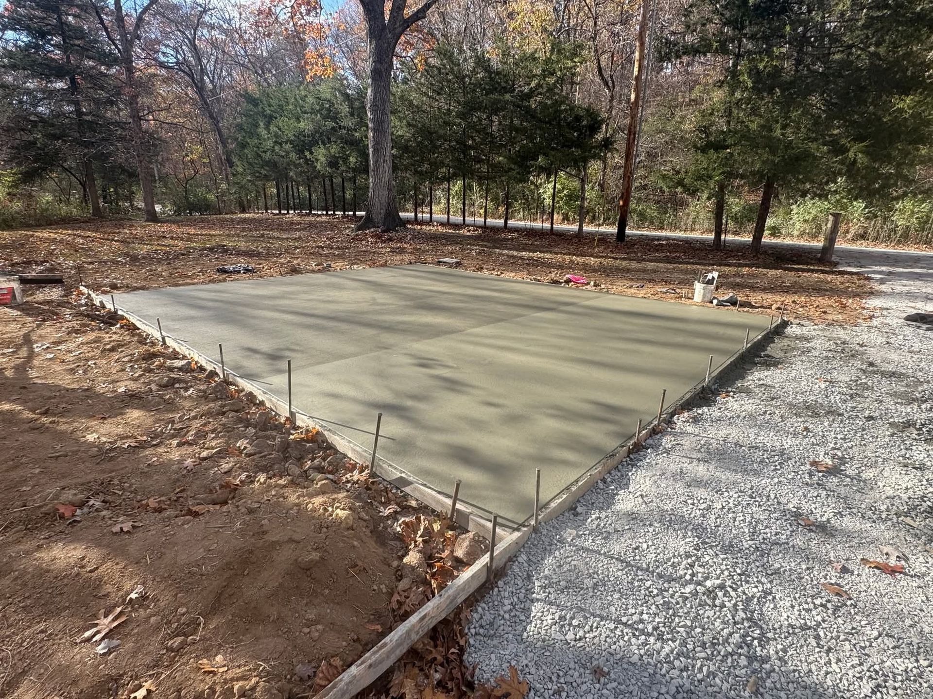 Fresh concrete slab under construction beside a gravel path in a wooded yard