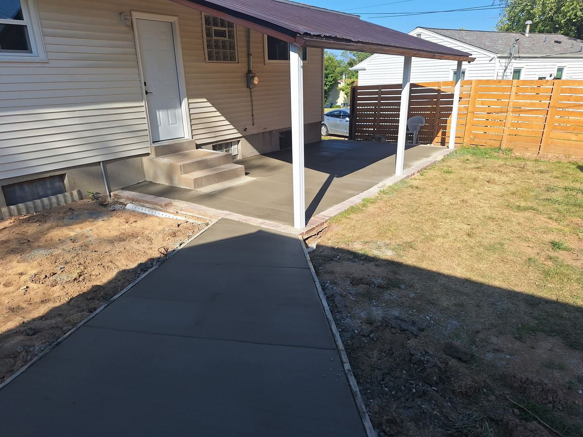 Concrete walkway leading to a house entrance with a covered patio and fenced yard