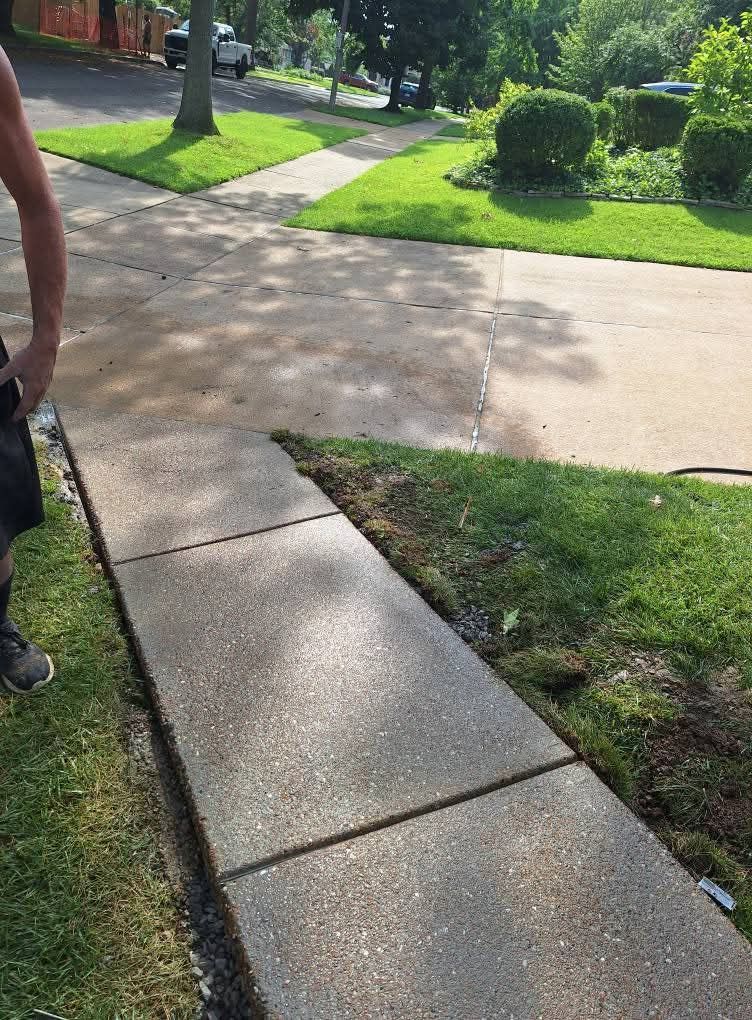 Concrete sidewalk beside a grassy suburban street with trees and a partially visible person at left