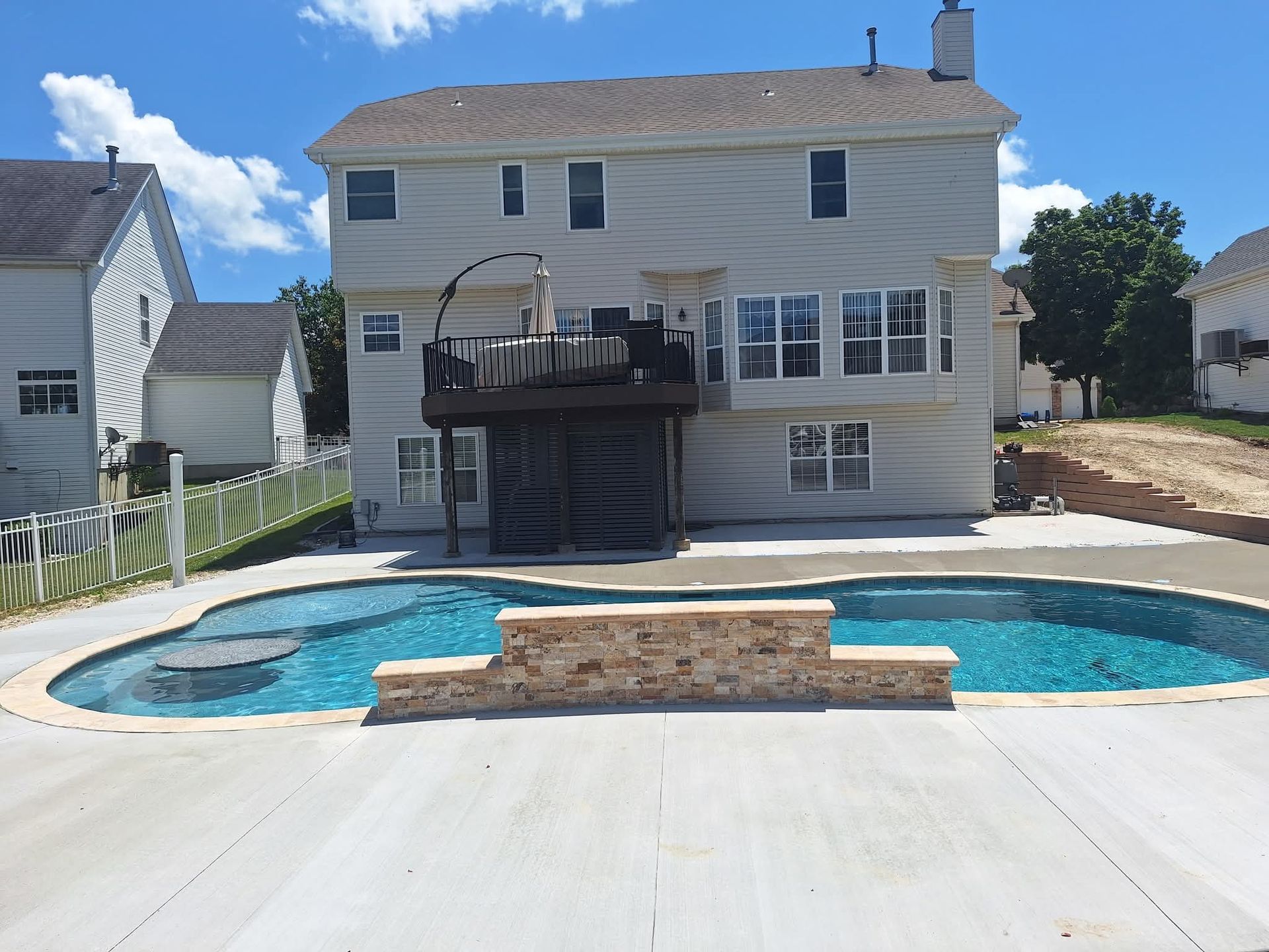 Backyard pool with a two-story house, deck, and concrete patio under a clear blue sky