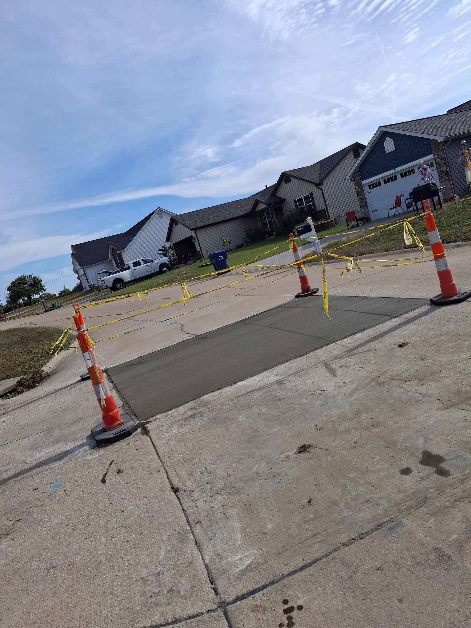 Barricaded street section with orange cones and yellow tape in front of suburban homes under a blue sky