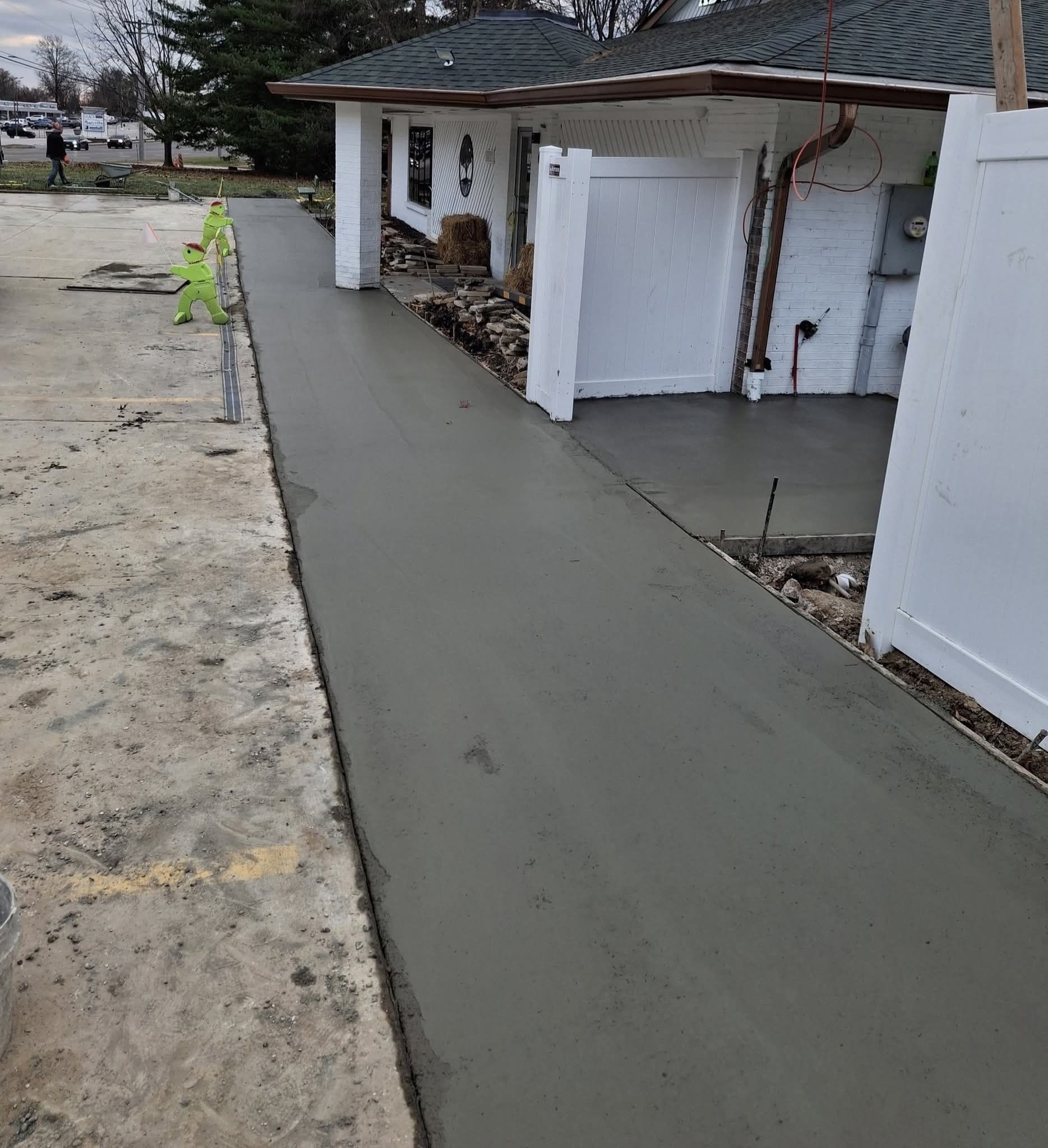 Fresh concrete walkway beside a white garage and fence, leading along a driveway.