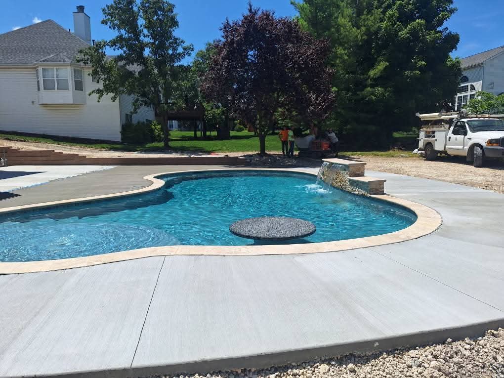 Backyard pool with curved deck, blue water, and a circular spa under trees in a suburban yard