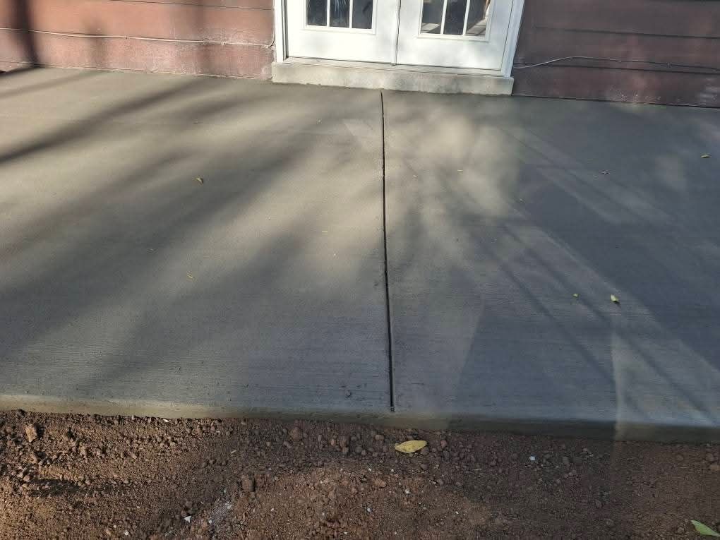 Concrete sidewalk with a central crack leading to double doors on a brick building.