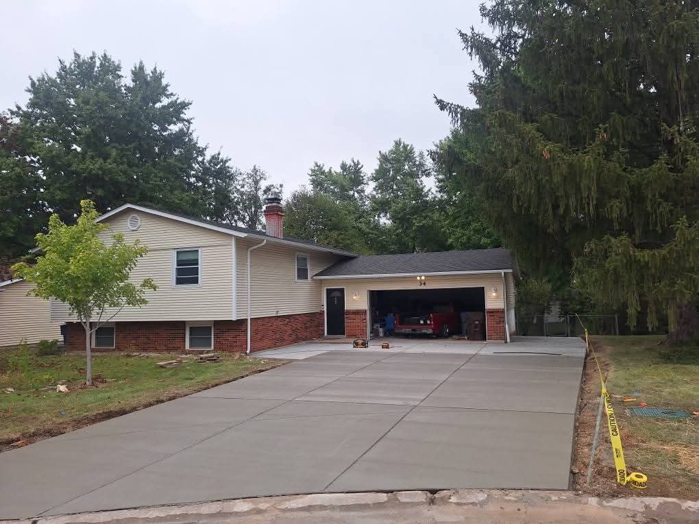 Suburban house with wide concrete driveway, open garage, and trees in front on a cloudy day