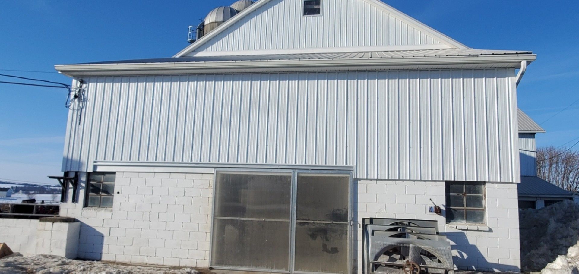 A white barn with vertical siding over a painted cinder block base, featuring sliding doors and small windows under a sky.